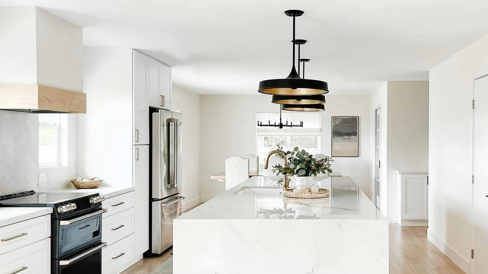 Modern all white kitchen with bold black and gold pendent lights hanging above a marble island