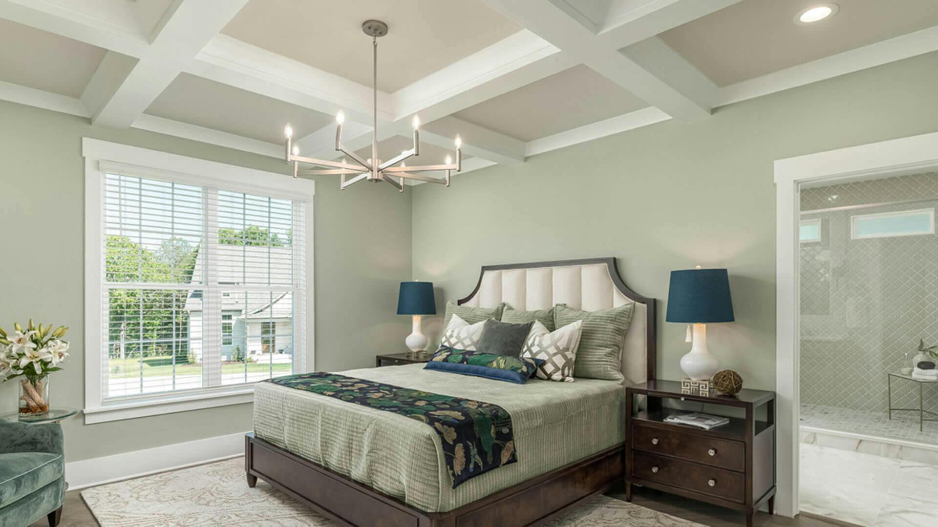 A bedroom with light sage green walls and bedding, featuring a white chandelier above the bed