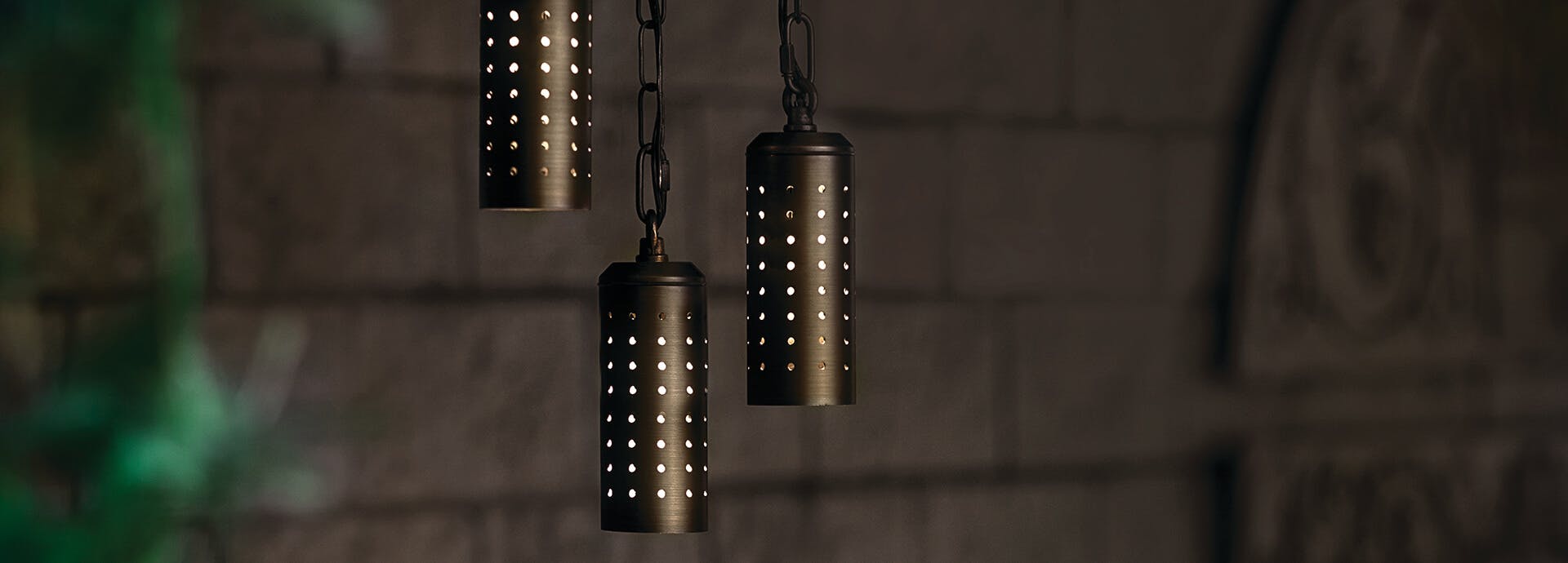 Close-up of three lit Twinkler pendants in centennial brass hanging against a brick wall