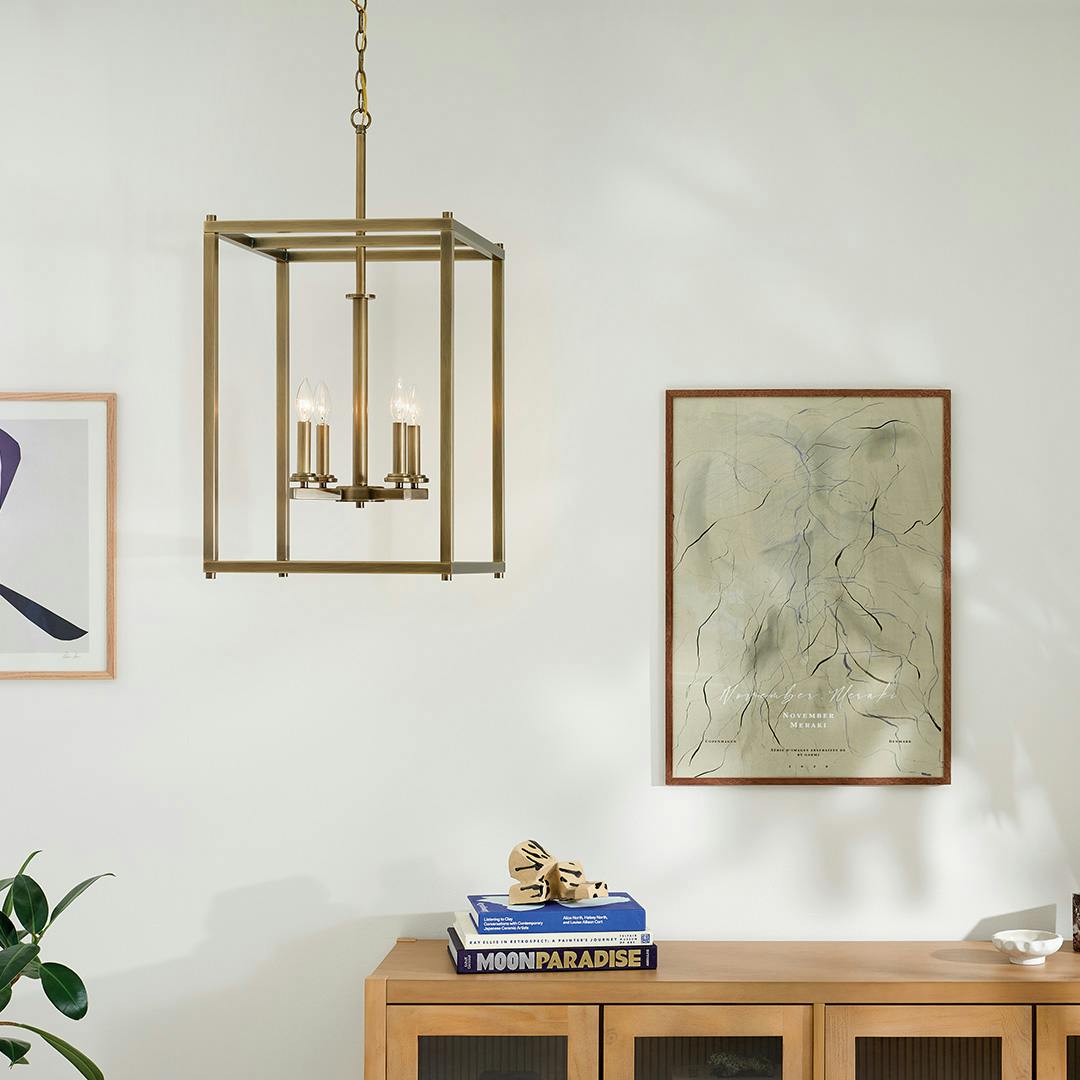 The Crosby 31" 4-Light Foyer Pendant with Clear Glass in Natural Brass hung in front of furniture and wall