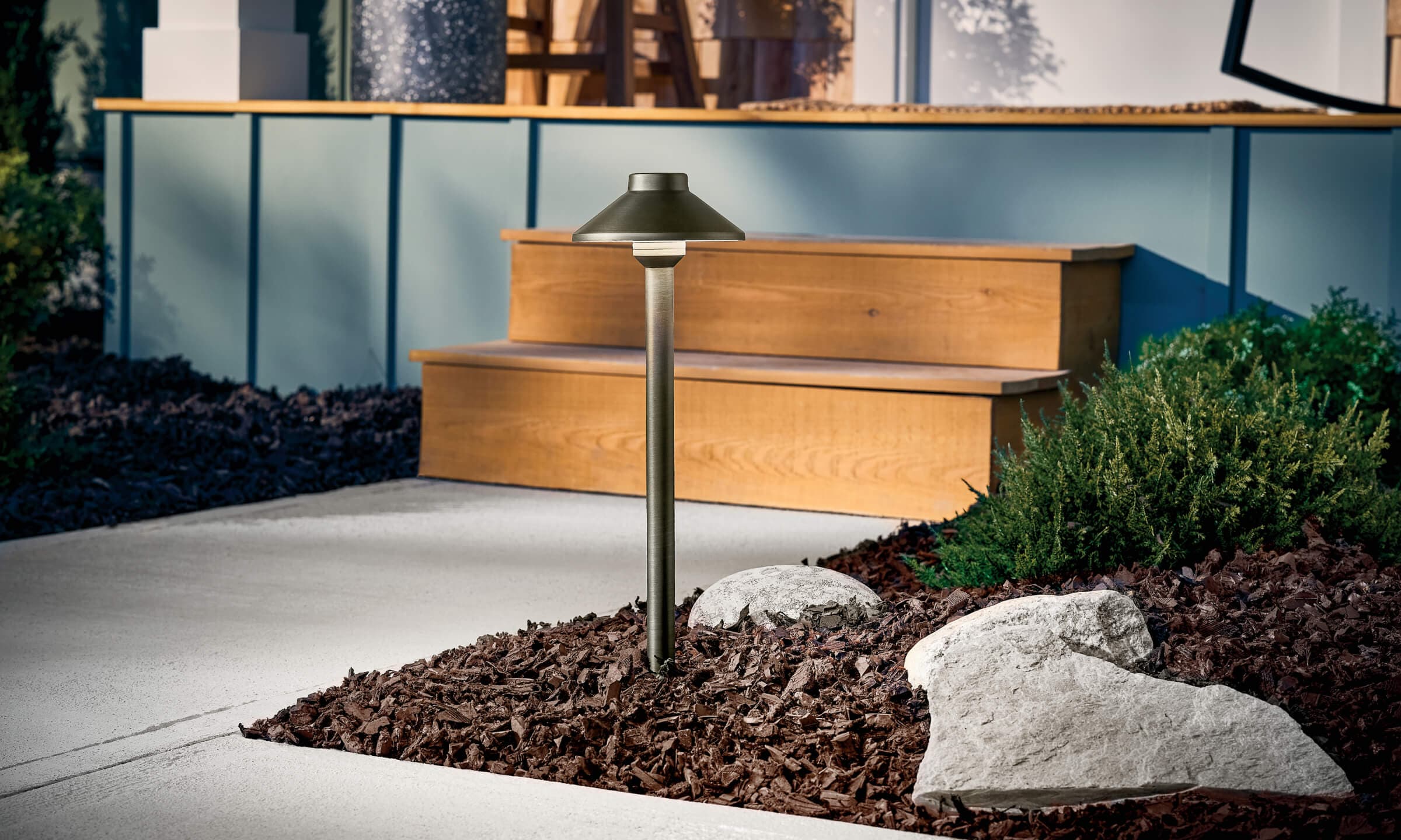 Detail shot of a Stepped Dome Path Light in landscape with mulch lighting a sidewalk turned on during the day 