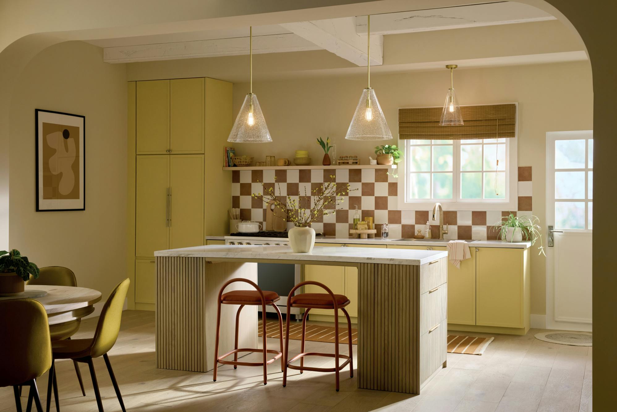 A kitchen with two Everly pendant lights above a kitchen island and one Everly pendant above the kitchen sink all turned on during the day 