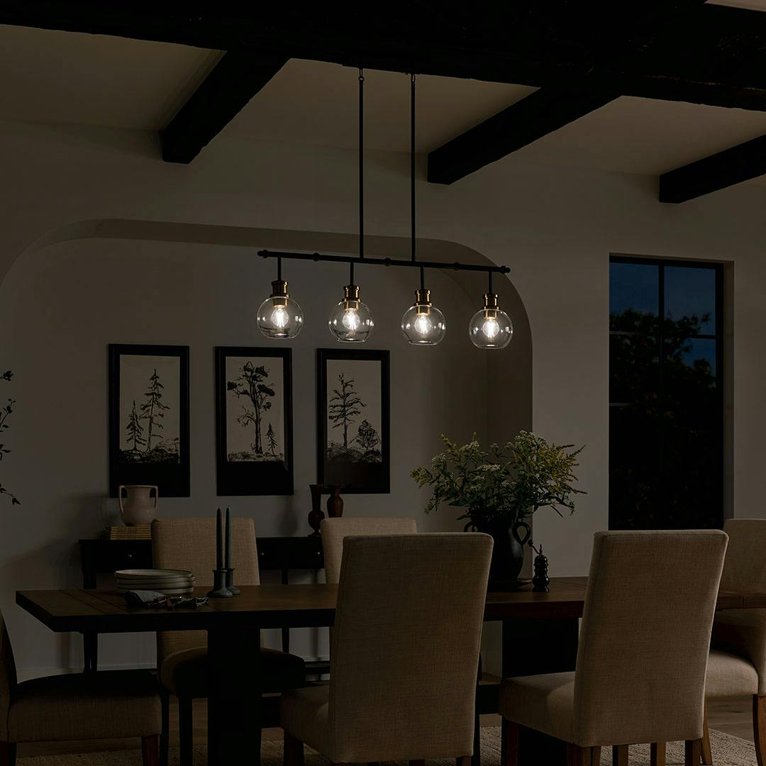 Dining room at night with the Clove 4 Light Linear Chandelier in Black and Brushed Natural Brass