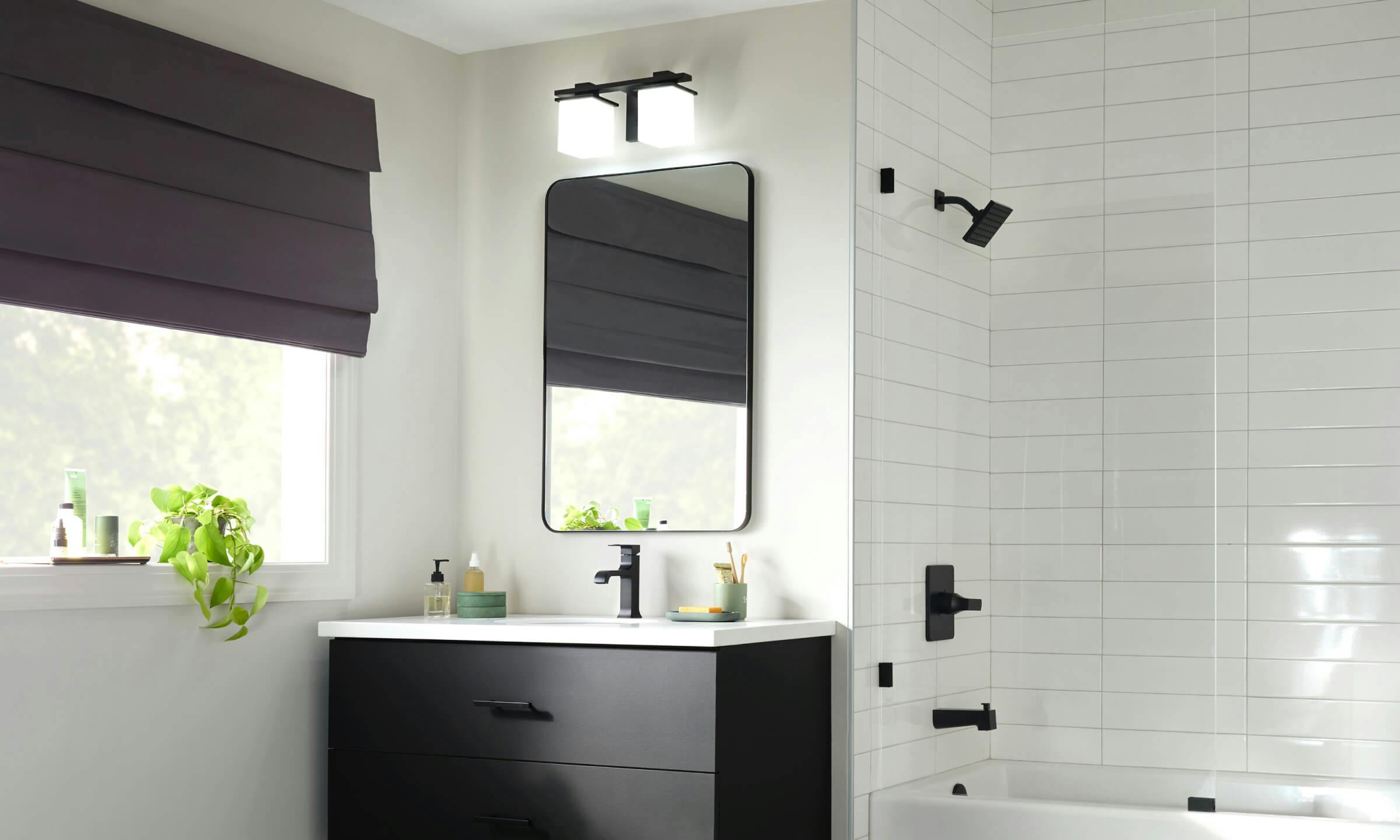 A bathroom lit with a Tully sconce with a black finish matching the Delta faucets and shower heads during the day 