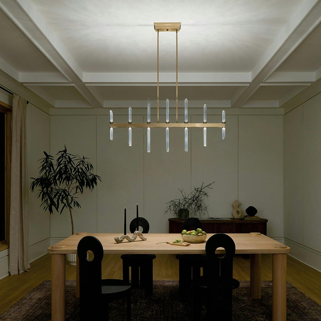 Night time dining room featuring the Sycara 48.25 Inch 14 Light LED Linear Chandelier with Faceted Crystal in Champagne Bronze on a white background