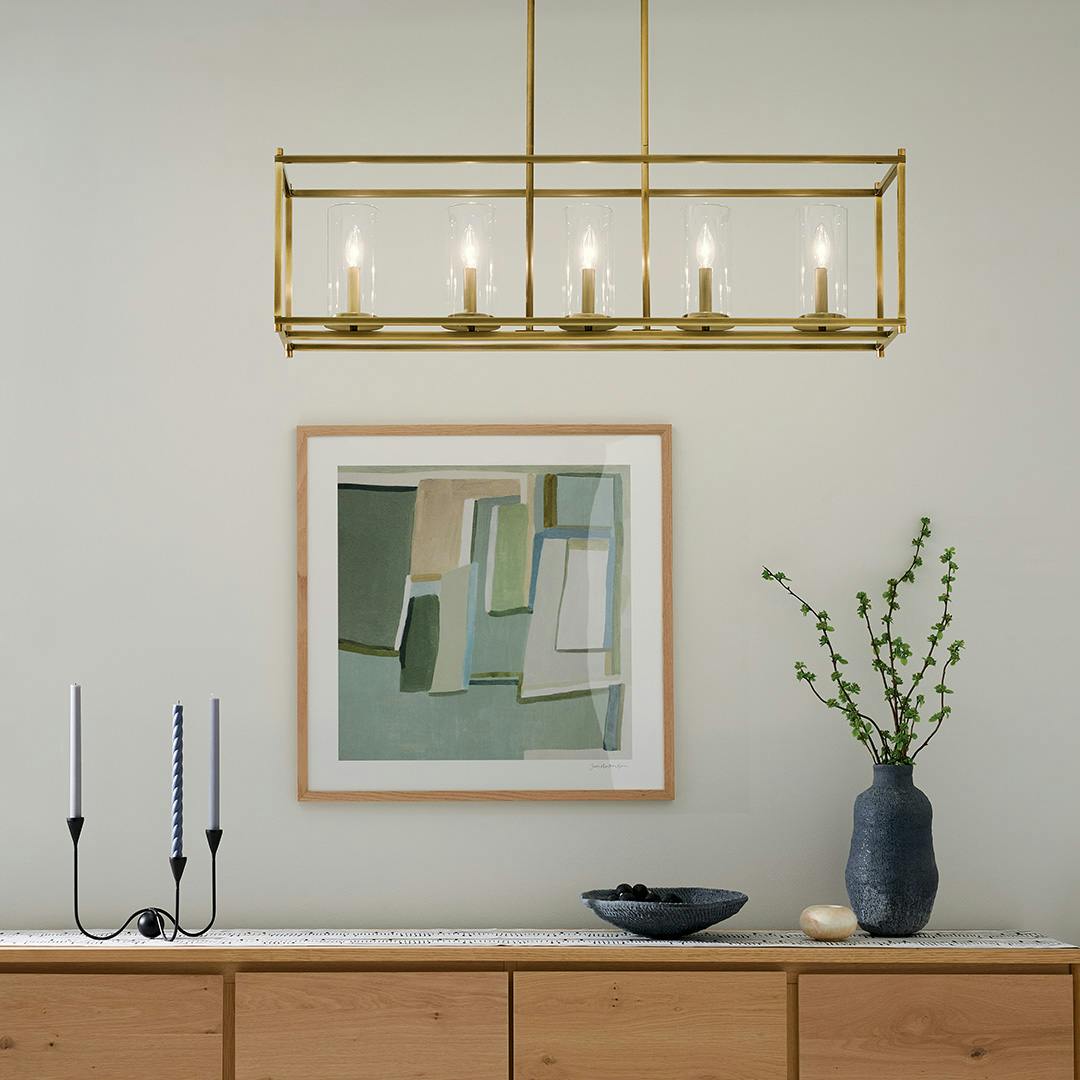 The Crosby 41.5" 5-Light Linear Chandelier with Clear Glass in Natural Brass hung in front of furniture and wall