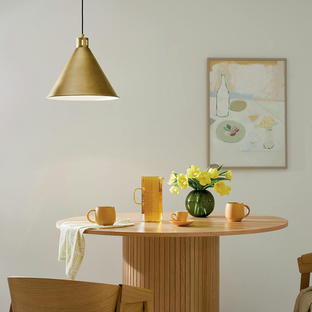 The Zailey 14.25" 1-Light Cone Pendant in Natural Brass hung in front of furniture and wall